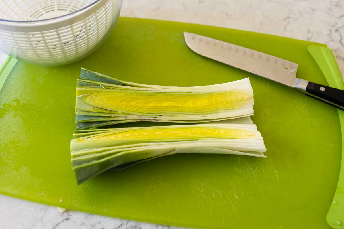 The leek has been sliced in half the long way on a cutting board.
