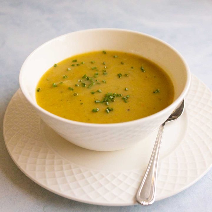 A white bowl of creamy Irish potato soup has fresh chives sprinkled on top and a spoon on the side.