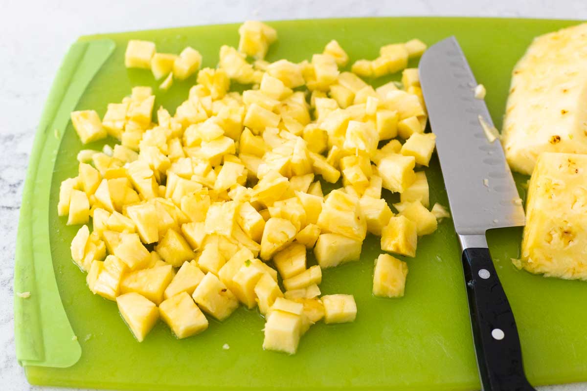 The pineapple is on a cutting board next to a chef knife.