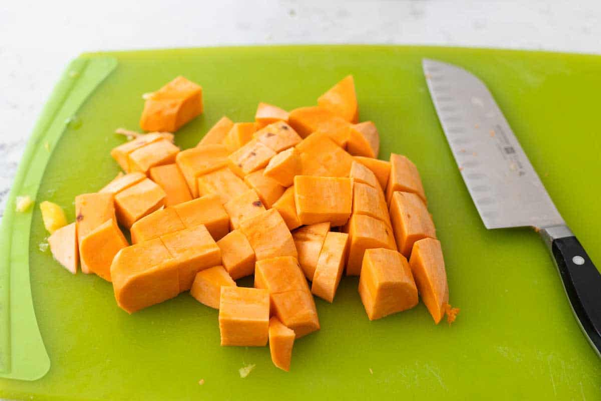 The sweet potato chunks are on a cutting board next to a chef knife.