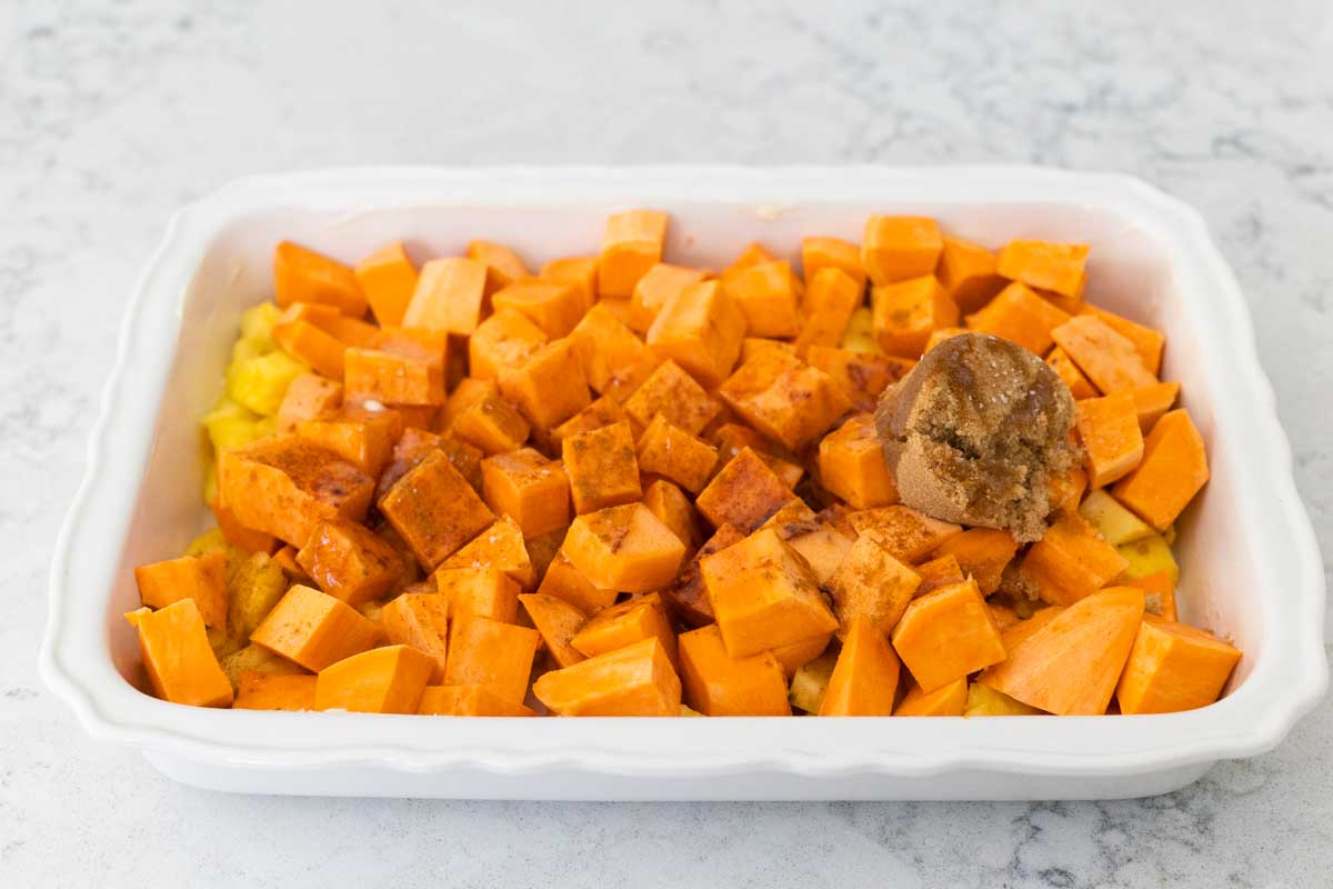 The sweet potatoes and pineapple have brown sugar and melted butter sprinkled over the top in a white casserole dish.