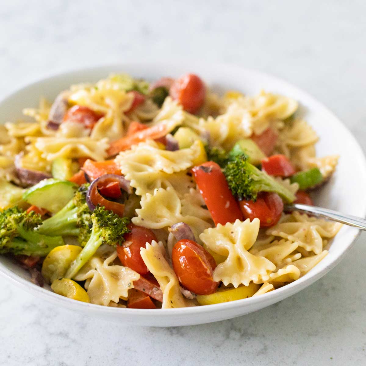 The vegetables have been tossed with farfalle pasta and are served in a white bowl.