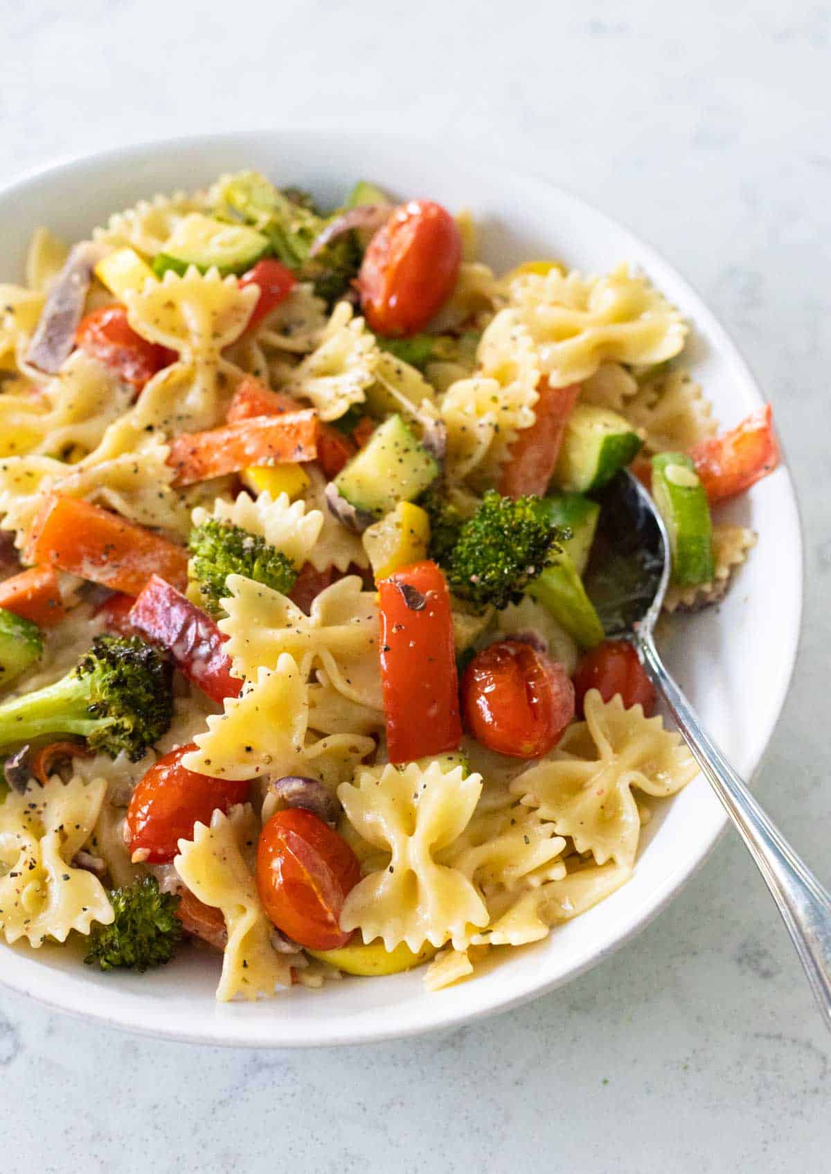 The finished farfalle primavera is in a large white bowl with a spoon.