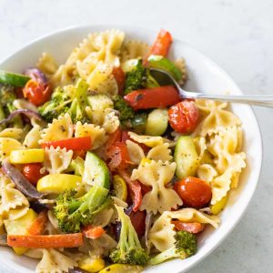 A white bowl is filled with farfalle pasta and fresh vegetables.