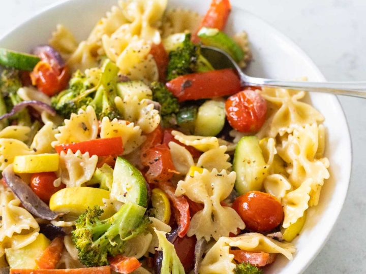 A white bowl is filled with farfalle pasta and fresh vegetables.