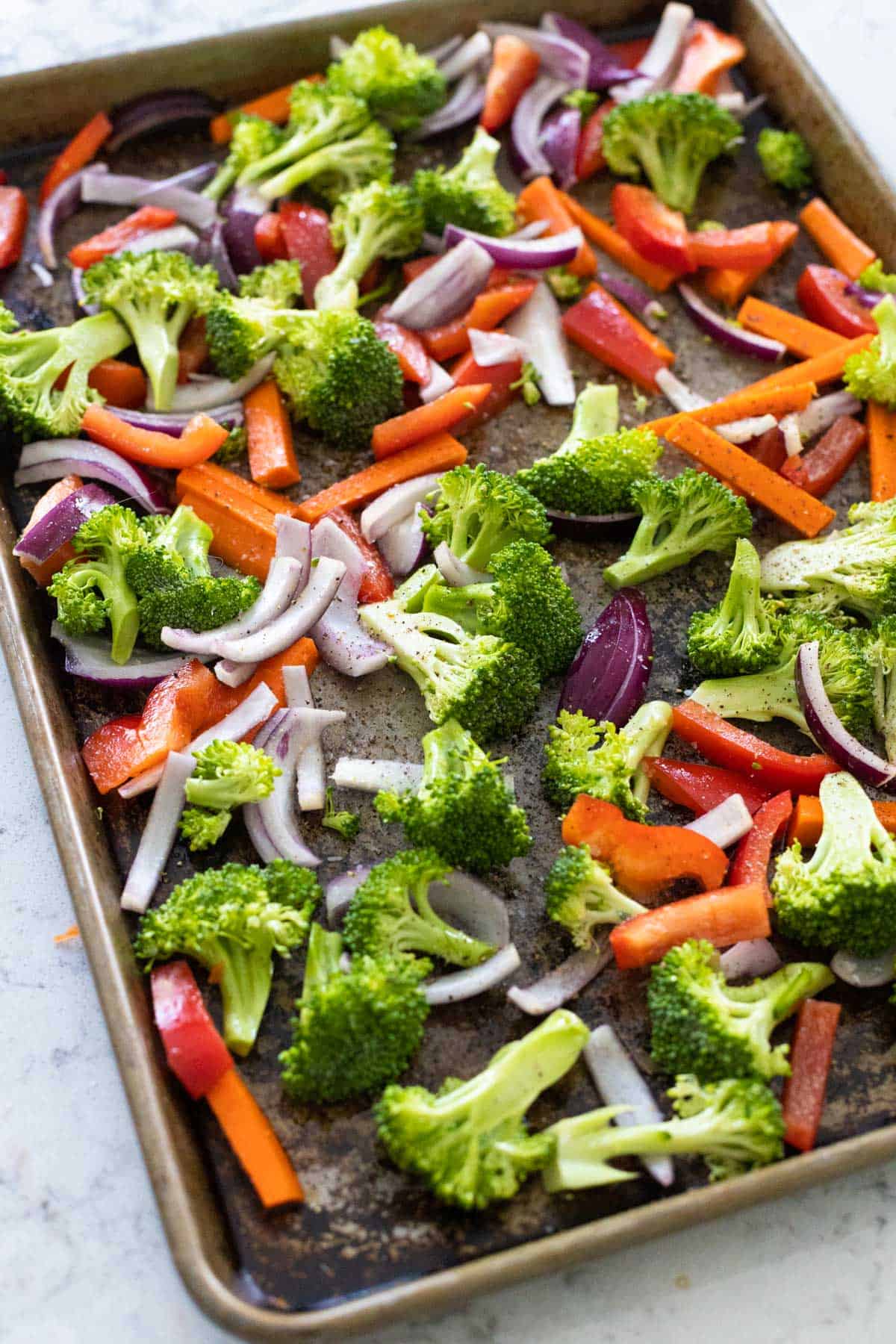 The broccoli and carrots are tossed in olive oil on the baking sheet.