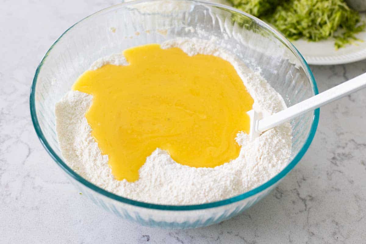 The mixing bowl filled with flour has the beaten eggs poured over the top.