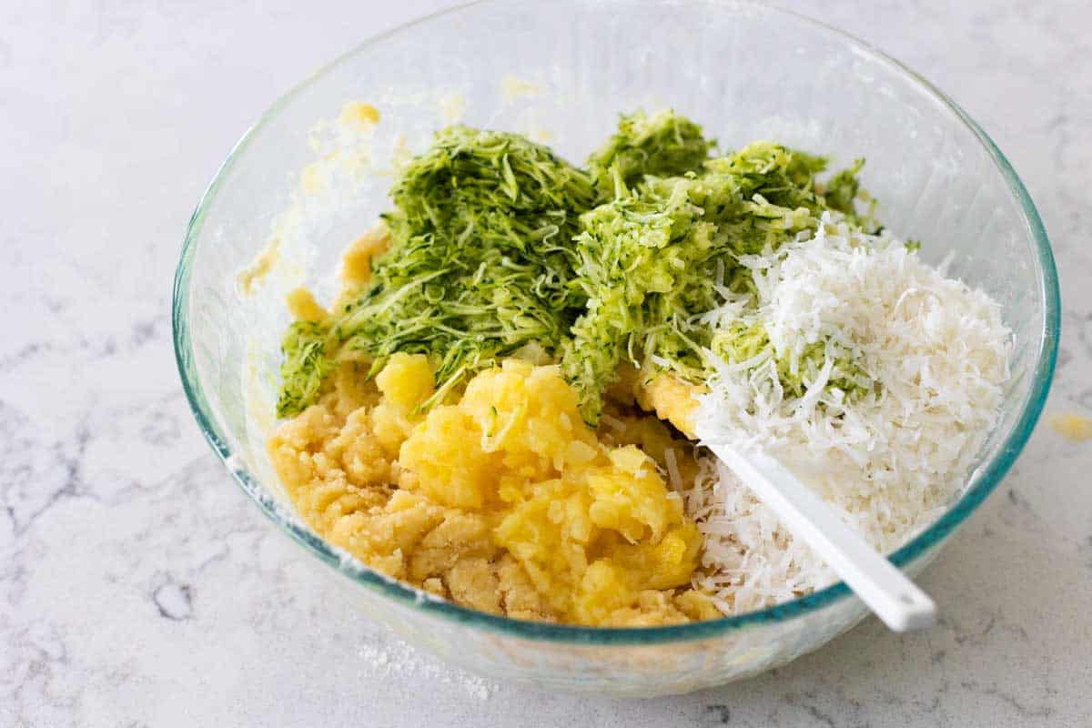 The mixing bowl has the pineapple, zucchini, and coconut on top.