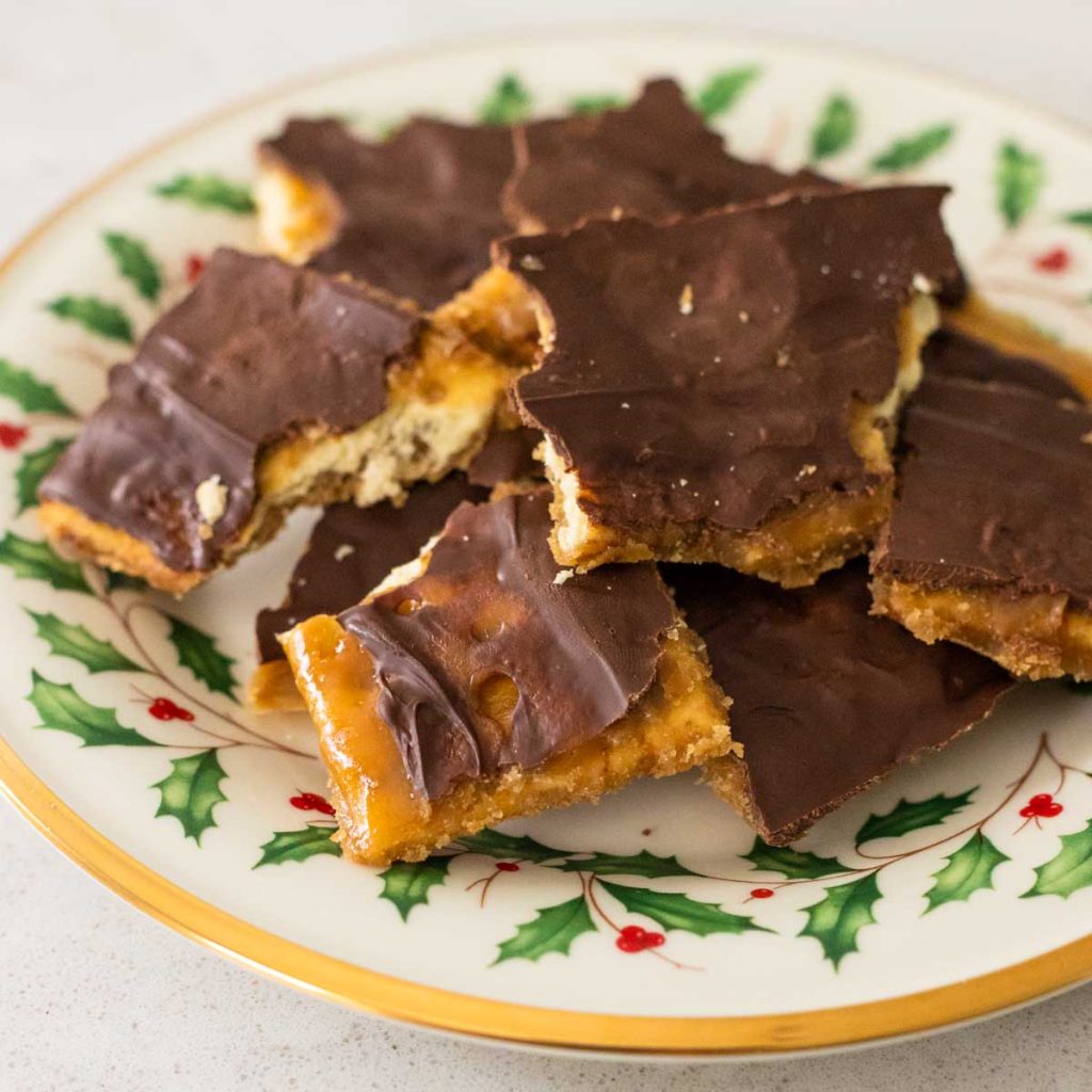 A Christmas holly plate has a pile of choclolate covered saltine cracker toffee.
