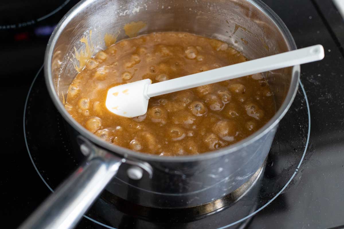 The toffee sauce is bubbling in a saucepan. A white spatula is stirring it.