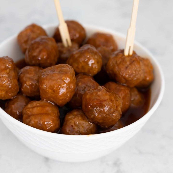 The white serving bowl is filled with sweet and sour meatballs in a rich glaze.