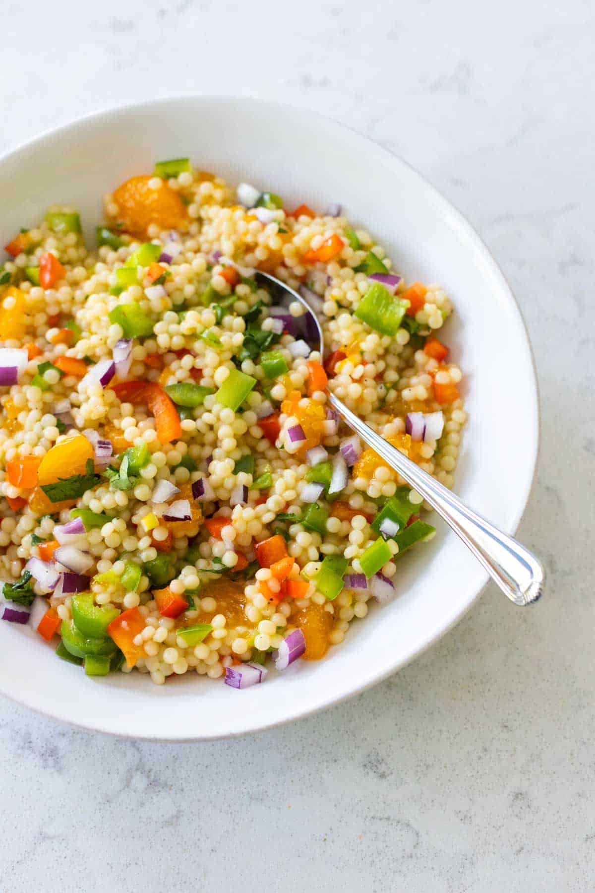 The finished salad is in a white bowl with a spoon. Colorful veggies and oranges are mixed throughout.