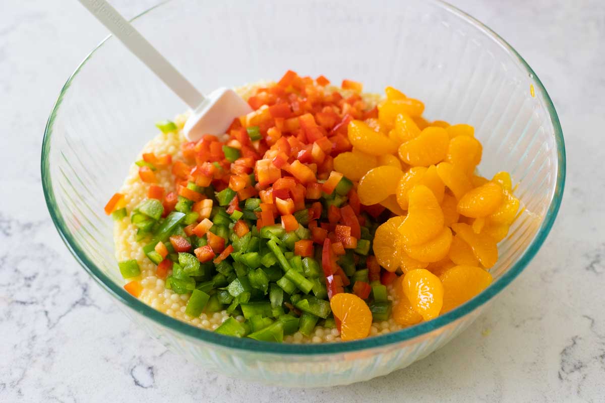 The diced peppers and orange segments are being stirred into the couscous