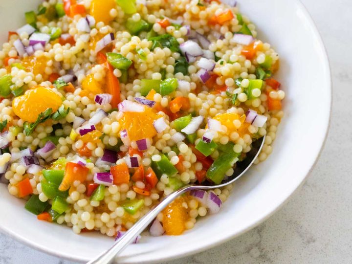 A white bowl filled with couscous salad. Oranges and bell peppers are peeking out of the mix.