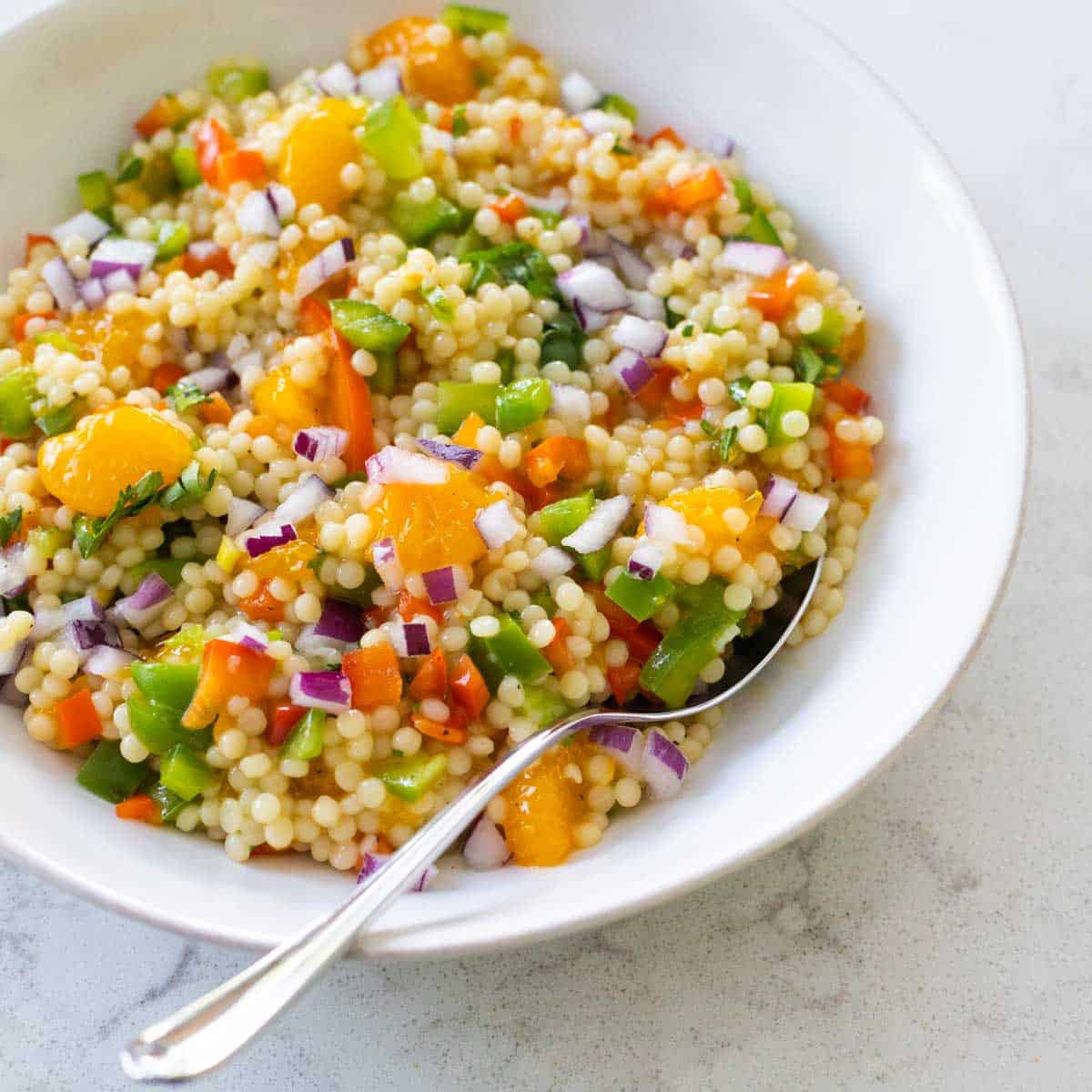 A white bowl filled with couscous salad. Oranges and bell peppers are peeking out of the mix.