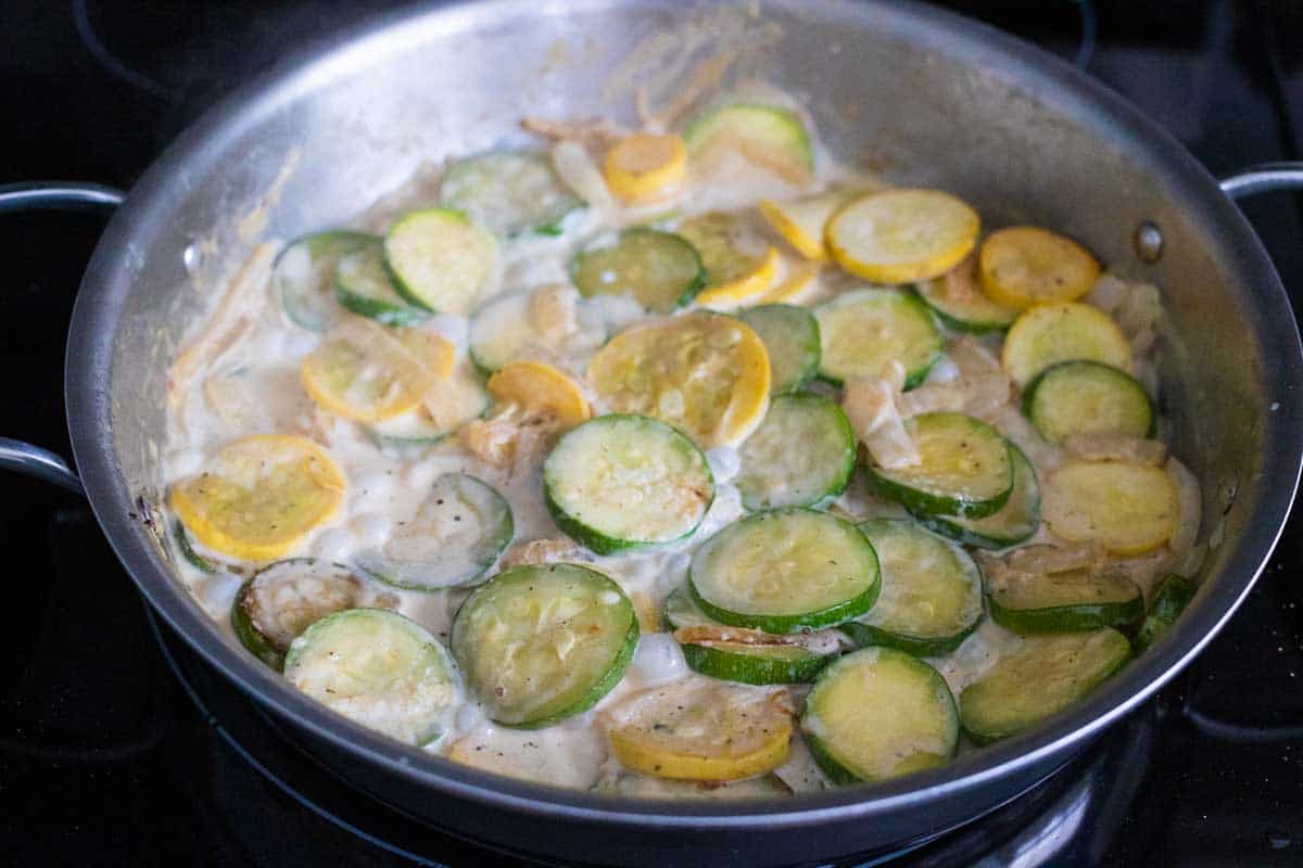 The cream sauce is bubbling all around the squash in the skillet.