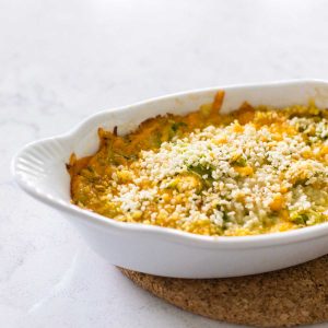 A white baking dish has baked zucchini gratin with breadcrumbs on top.