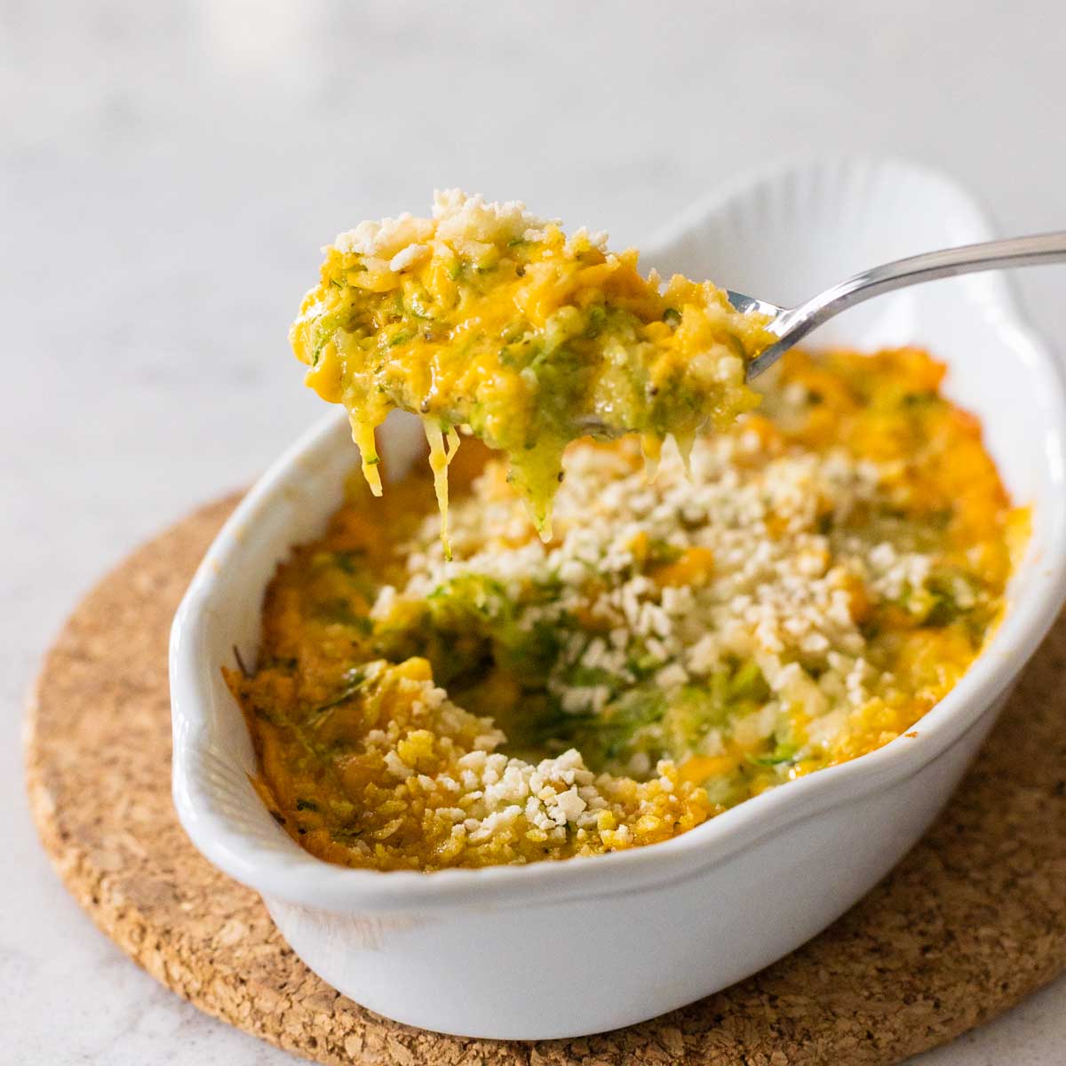 A spoon is pulling up a bite of the cheesy zucchini gratin so you can see the melted cheese pull.
