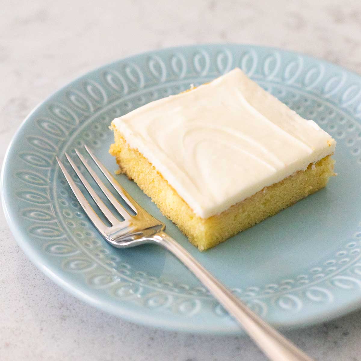 A square piece of almond cake has a smooth layer of almond icing on top.