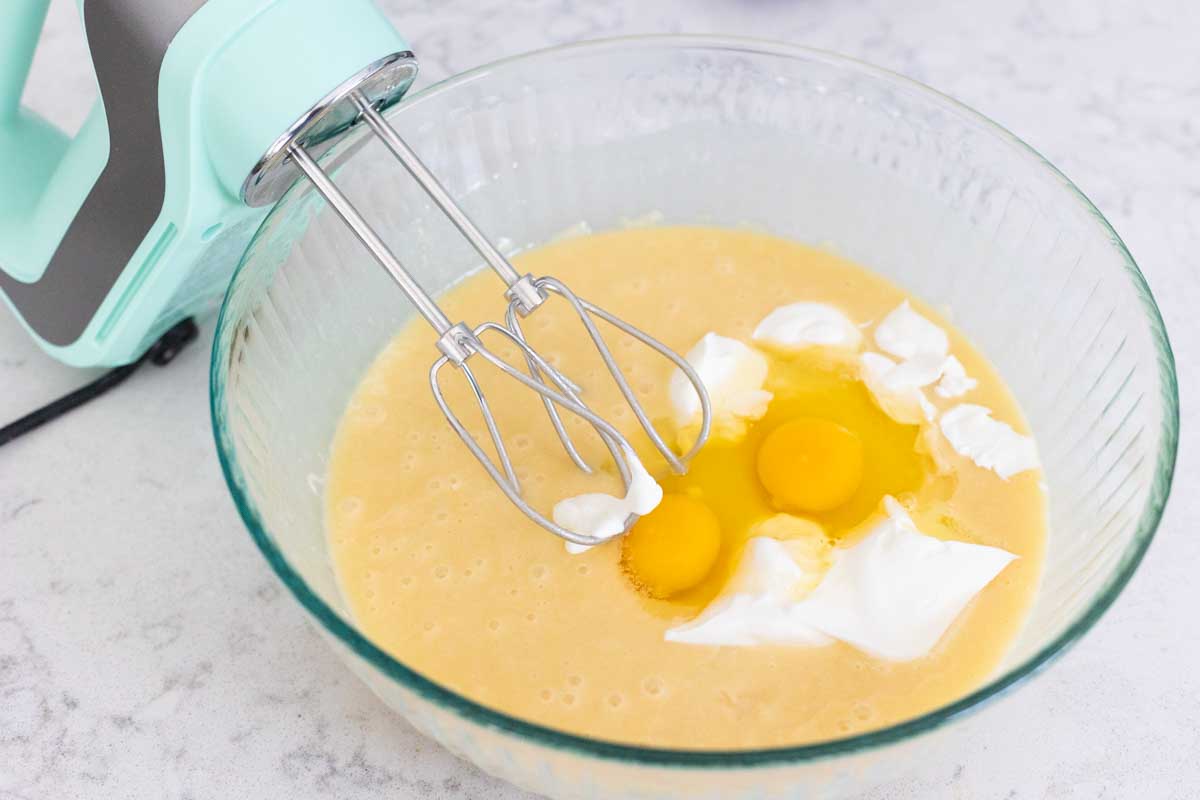 The batter has been mixed and then the eggs and sour cream are added to it. The beater is ready to mix it together.