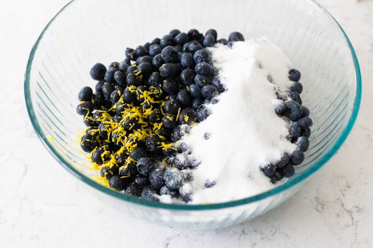 The blueberries are in a mixing bowl with sugar and lemon zest.