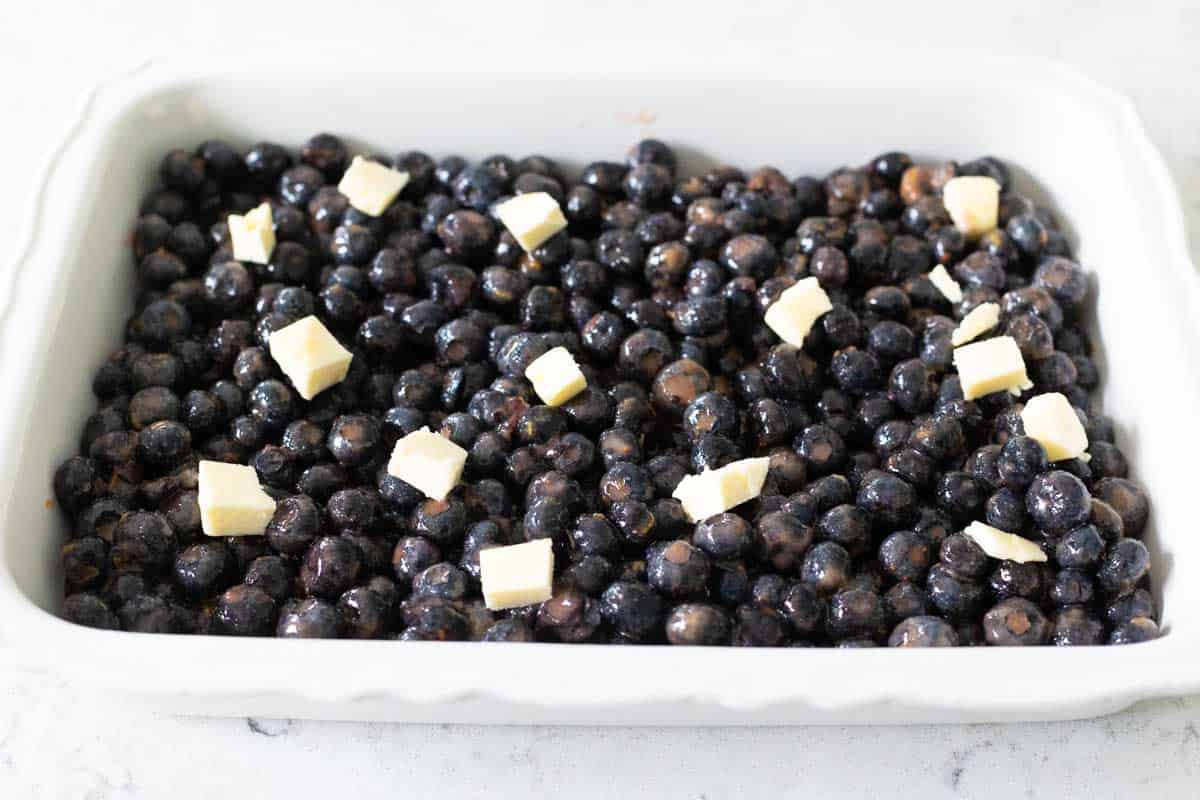 The blueberry filling has been spread into a 9x13-inch baking dish. Little squares of butter are scattered over the top.