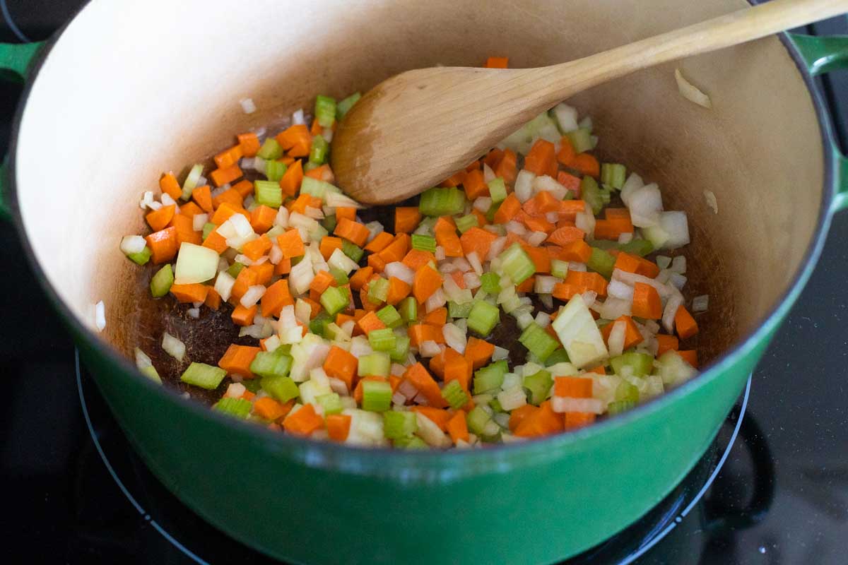 The carrots, onion, and celery are sauteeing in the Dutch Oven with a wooden spoon stirring the mix.