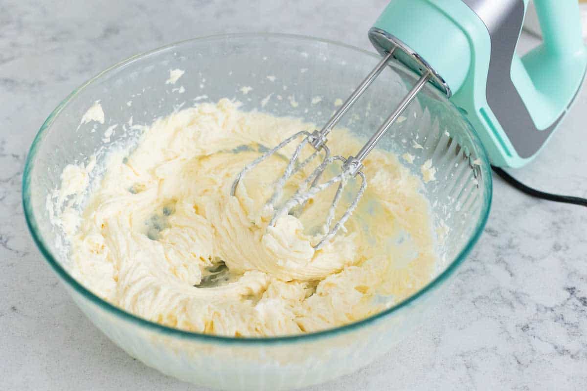 The cream cheese and sugar have been beaten with a hand mixer until smooth in a large mixing bowl.