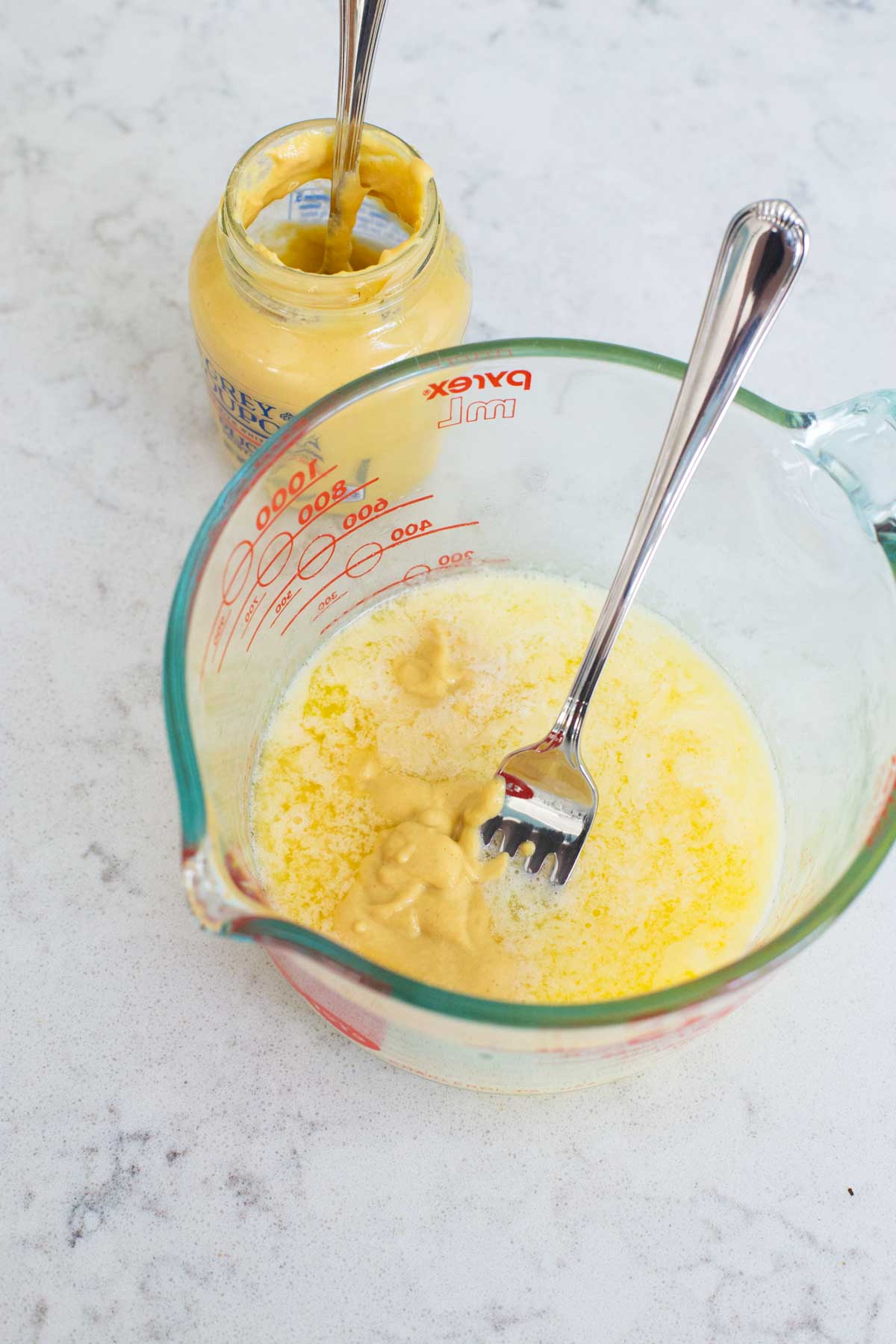 The melted butter and Dijon mustard are being mixed together in a liquid measuring cup with a fork.