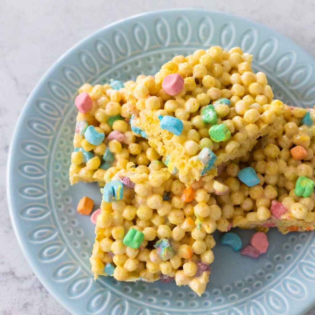 A blue plate has a pile of Mini Lucky Charms Krispie Treats with rainbow marshmallows.