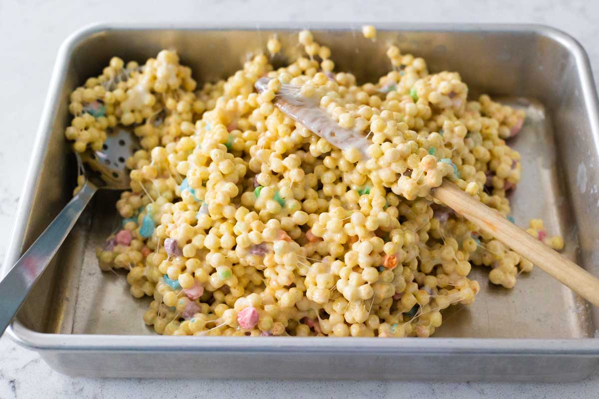 The baking pan has a clump of the krispie treats mixture ready to be smoothed out.