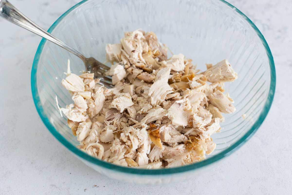 A rotisserie chicken has been shredded and the meat is in a mixing bowl.
