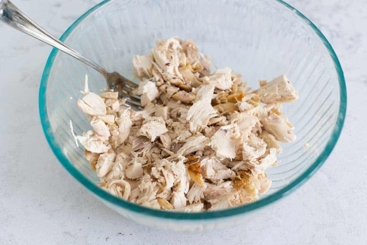 A rotisserie chicken has been shredded and the meat is in a mixing bowl.