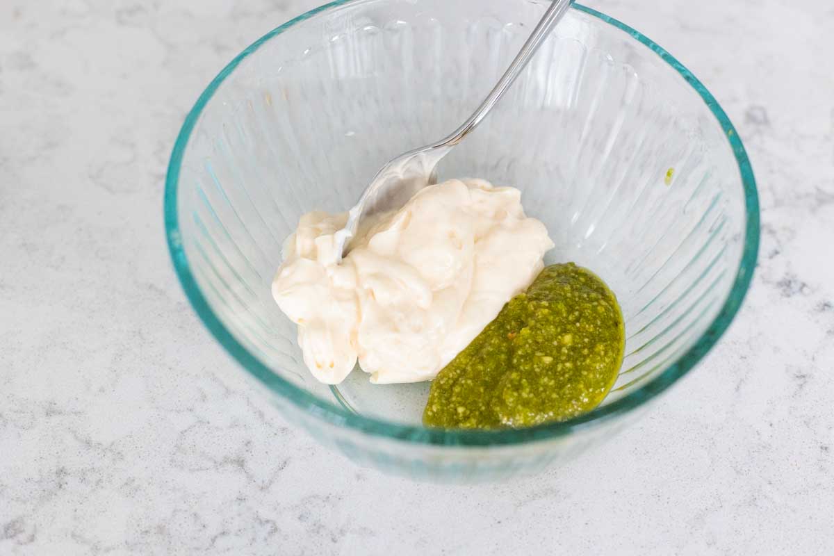 Mayo and pesto are in a mixing bowl with a spoon.