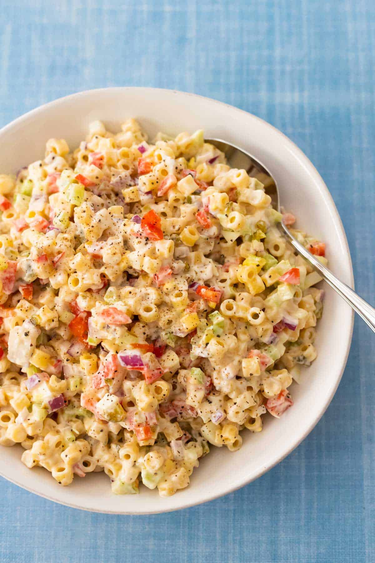 The finished pasta salad is in a white bowl with a spoon for serving.