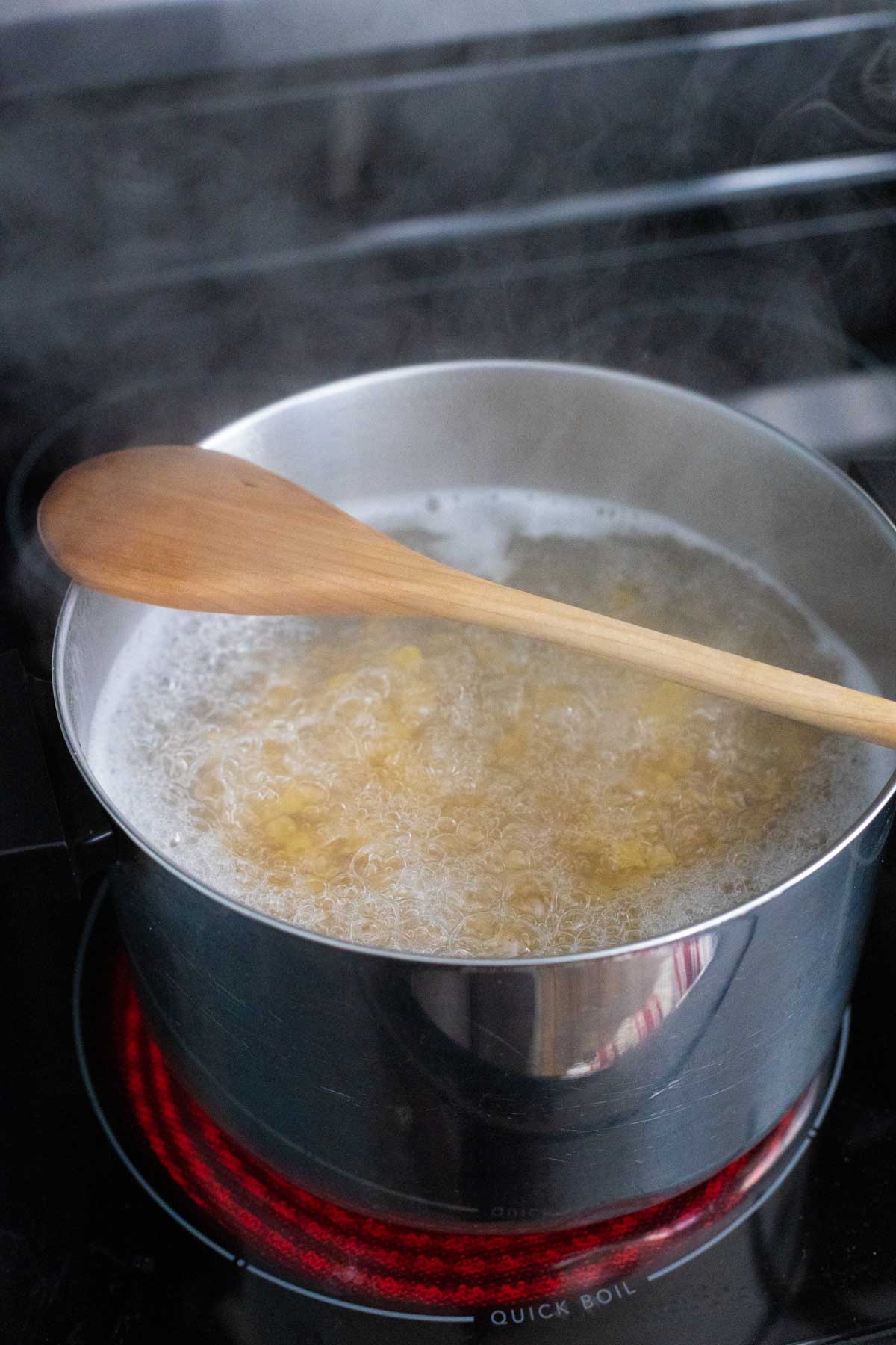 The pasta pot has a wooden spoon over the boiling water to prevent it from boiling over.