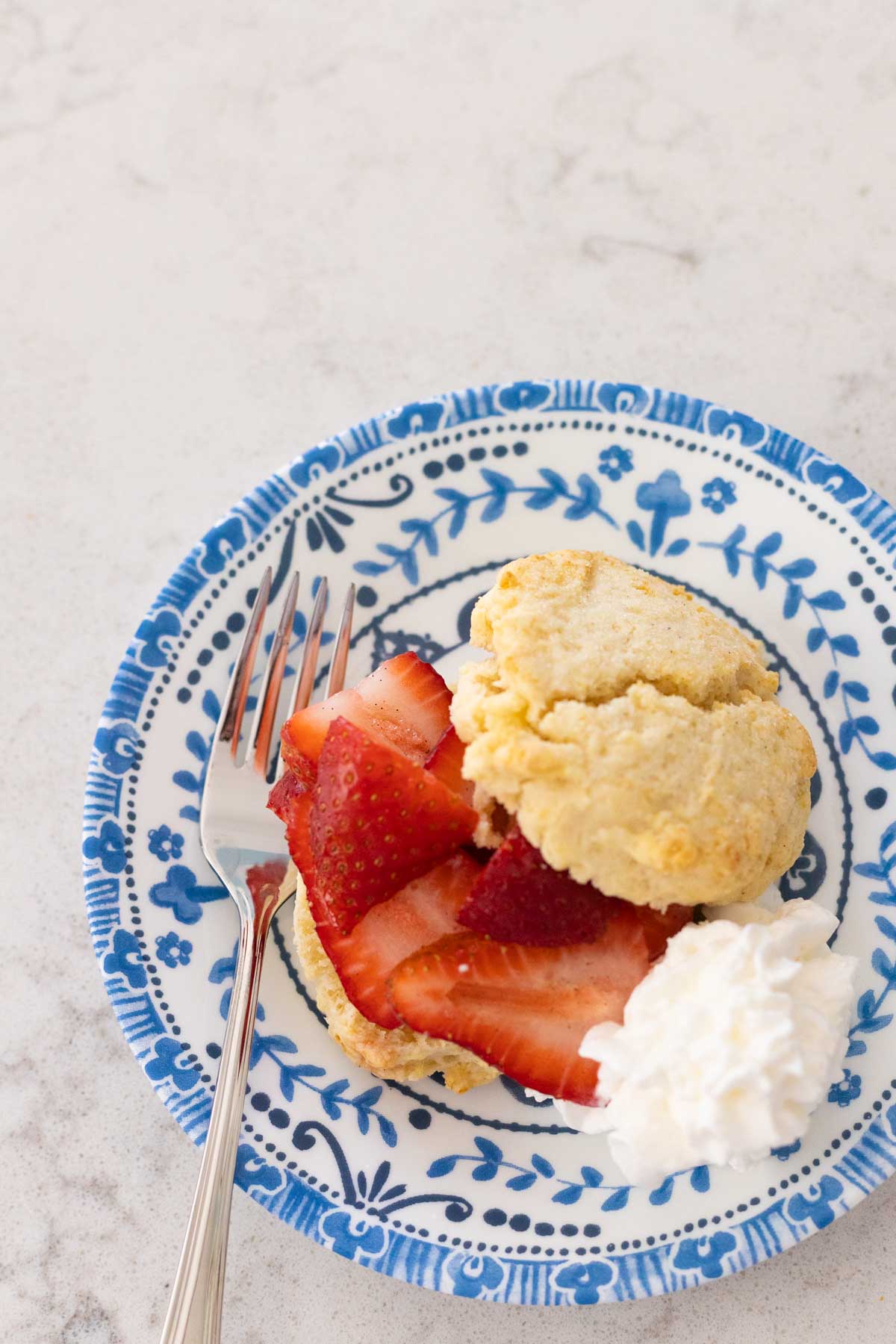 The shortcake has been split in 2. Fresh strawberries are on one half and a dollop of whipped cream is on the side.
