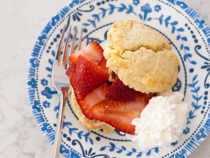 A classic strawberry shortcake has been split in half with fresh berries and whipped cream.