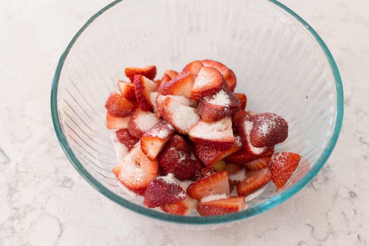 The strawberries are in a mixing bowl getting tossed with sugar.