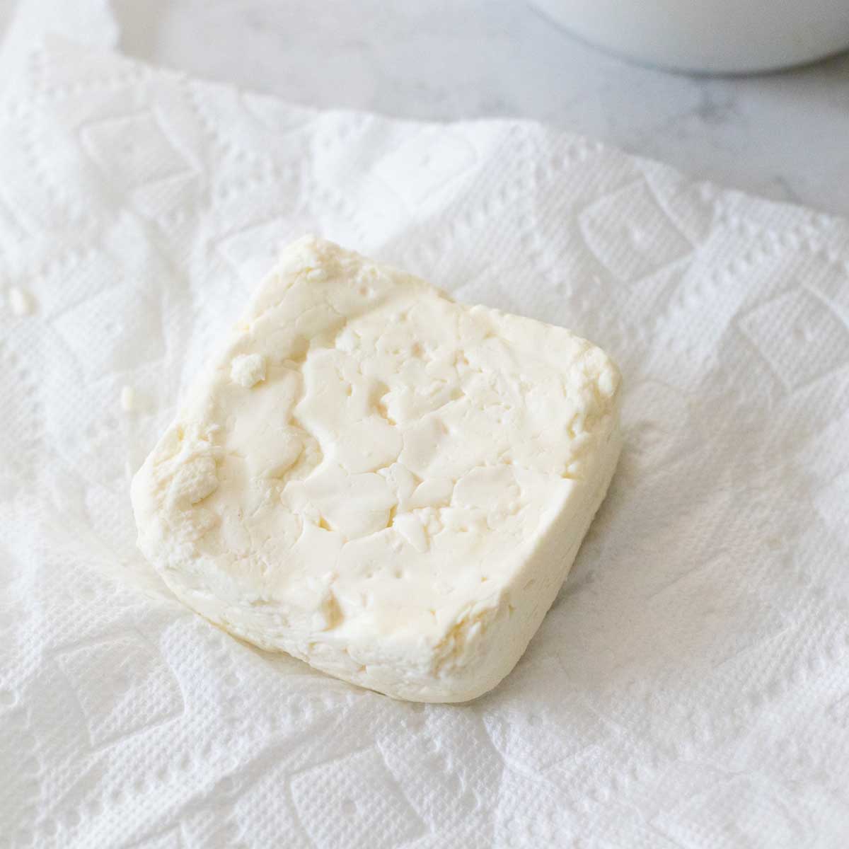 The square of feta cheese is being dried on paper towels.