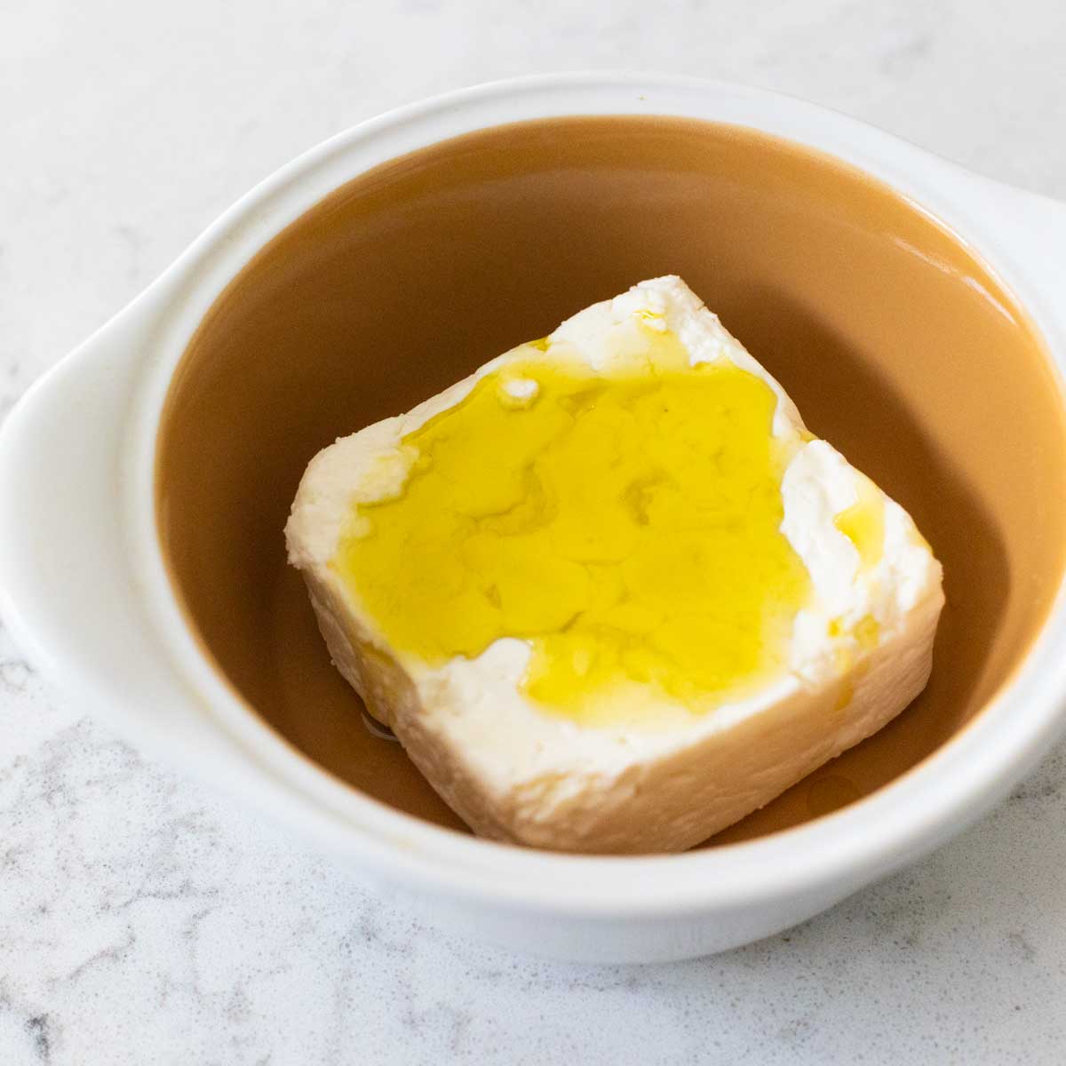 The feta cheese is in the baking dish and has the olive oil drizzled over the top.