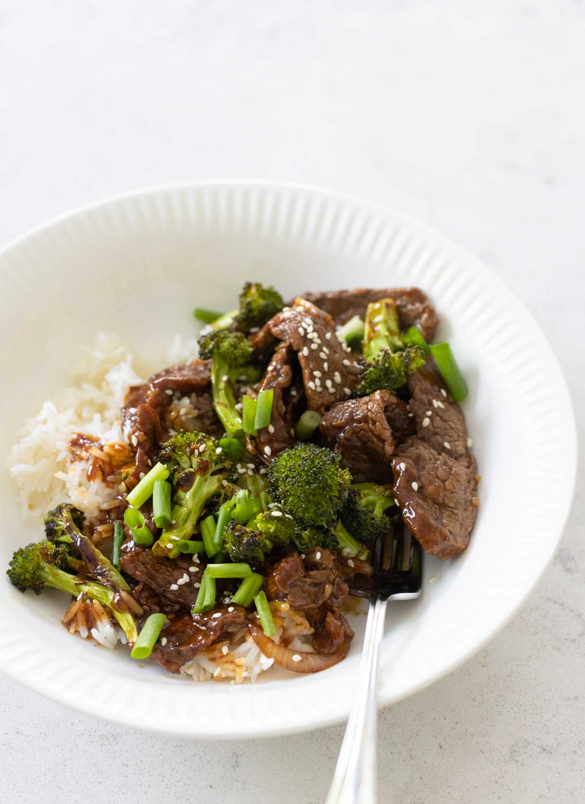 The beef and broccoli are in a white plate over a bed of rice.