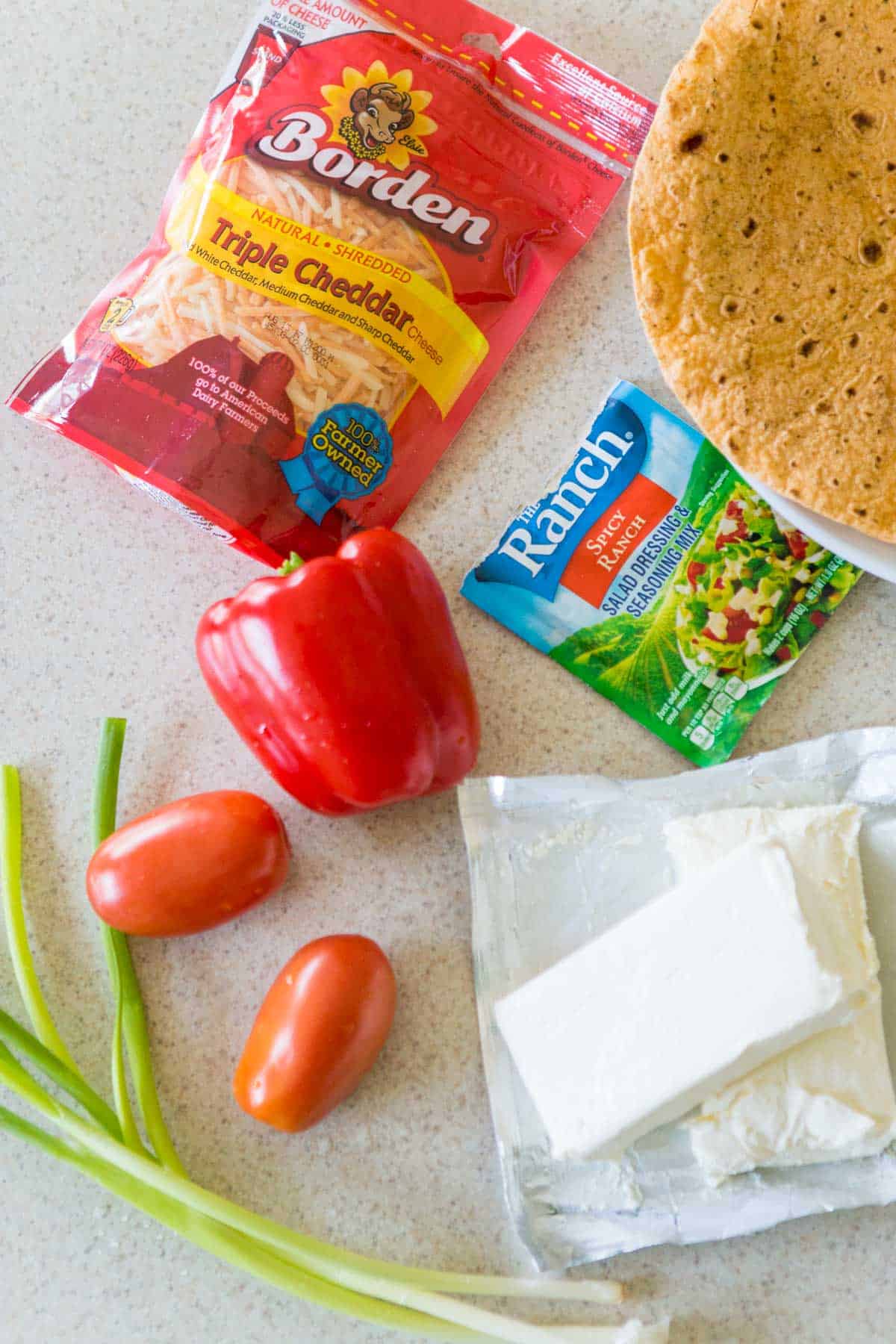 The tortillas, cheese, vegetables, and cream cheese are on the kitchen counter.