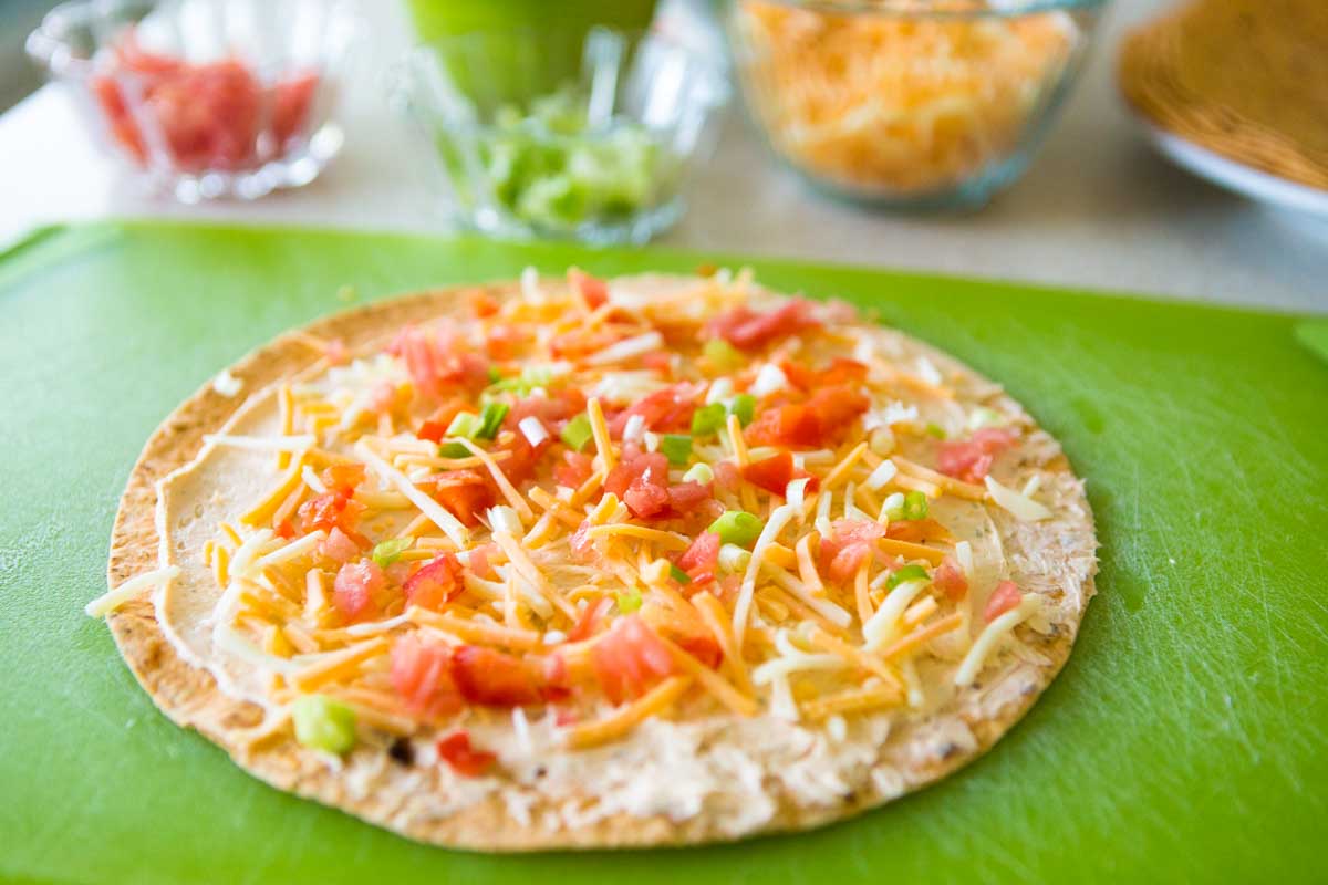 The cheese and veggies have been spread out on top of a tortilla.