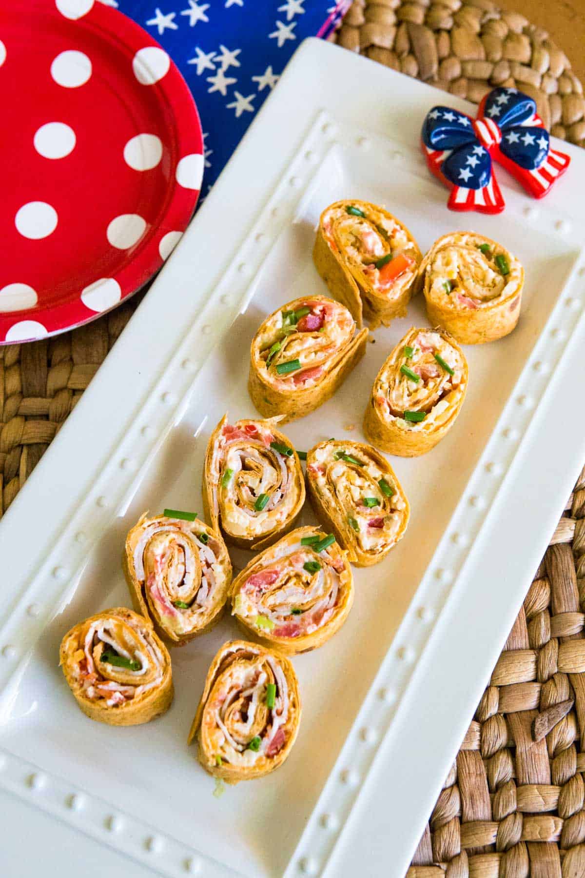 A white platter has the sliced pinwheels on top. A red white and blue bow is on the side.