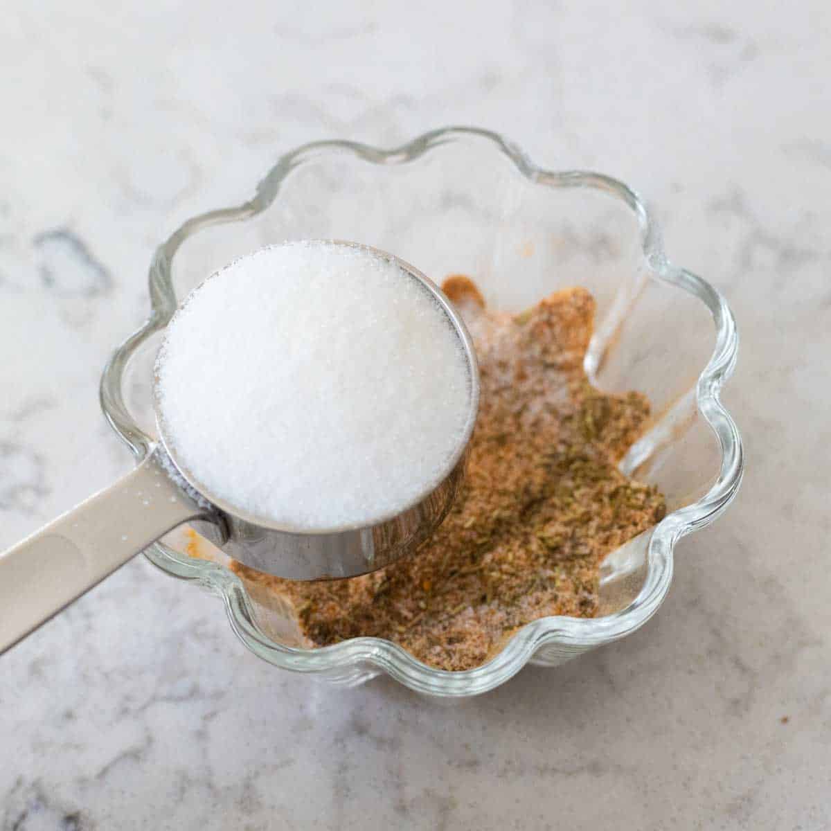 The measuring cup of table salt is being added to the seasonings.