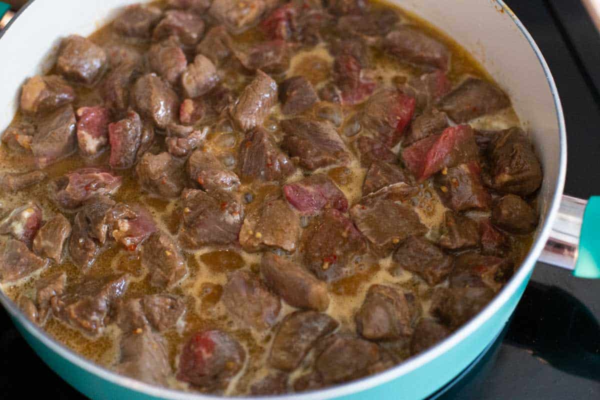 The marinated beef is in a large, deep skillet.