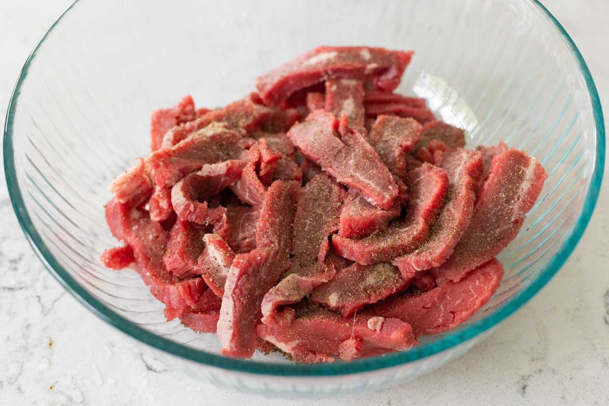 The flank steak has been seasoned in a mixing bowl.