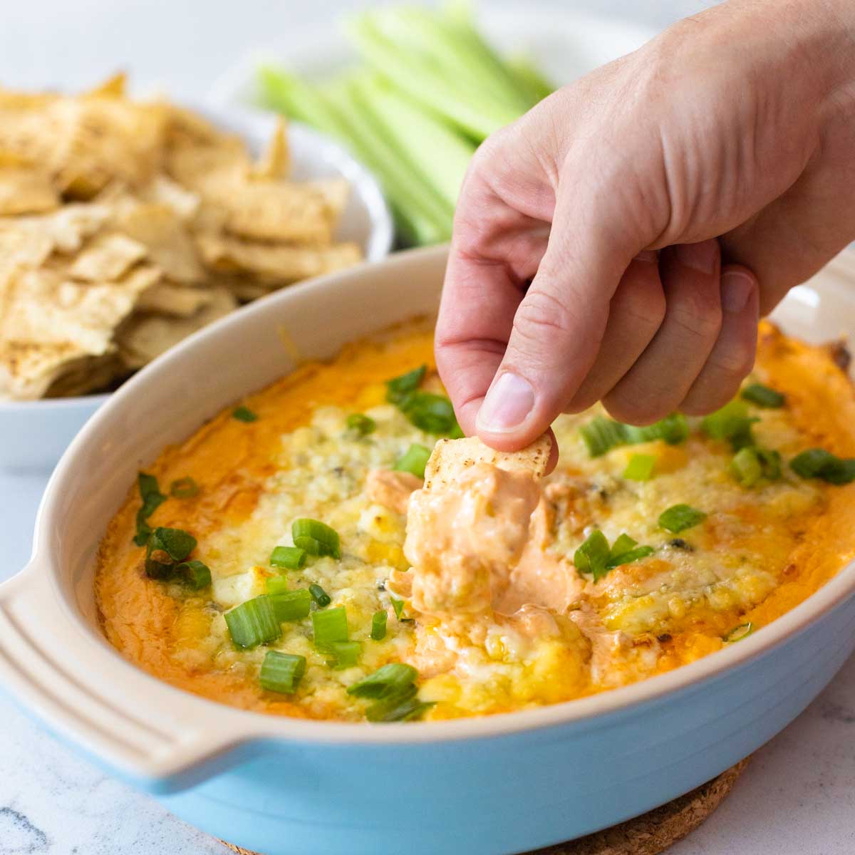 A man's hand is dipping a tortilla chip into the buffalo chicken dip.