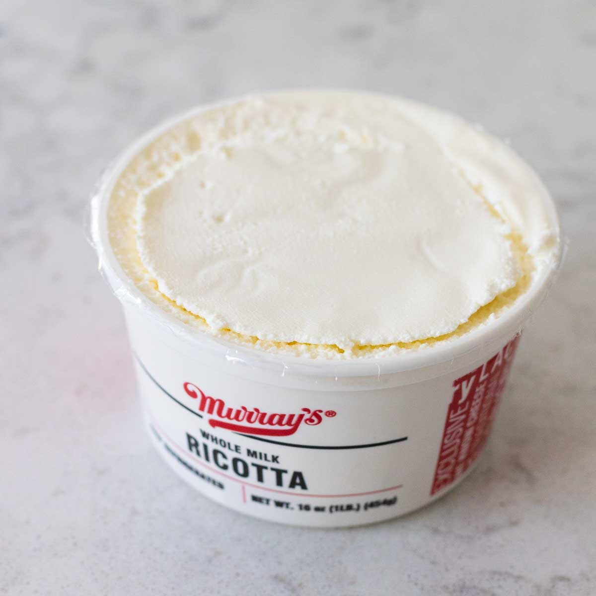 A close up look at the container of ricotta cheese shows the texture of the ingredient.